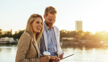 Walk with me Close up portrait of young businesspeople discussing about a project by the river. They are both happy. A man is holding a digital tablet while she is holding a coffee.